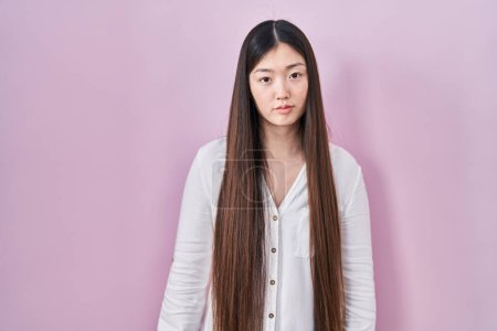 Photo for Chinese young woman standing over pink background relaxed with serious expression on face. simple and natural looking at the camera. - Royalty Free Image
