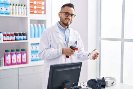 Foto de Joven hombre hispano farmacéutico escaneando pastillas botella en la farmacia - Imagen libre de derechos