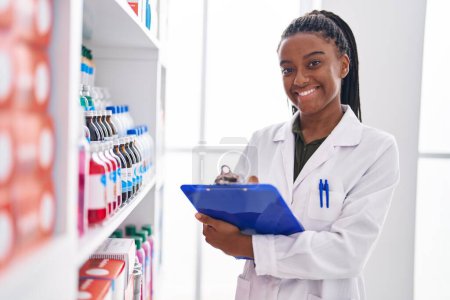 Photo for African american woman pharmacist smiling confident writing on document at pharmacy - Royalty Free Image