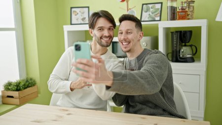 Téléchargez les photos : Deux hommes couple ayant appel vidéo boire un verre de vin à la salle à manger - en image libre de droit