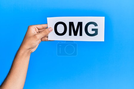 Photo for Hand of caucasian man holding paper with omg word over isolated blue background - Royalty Free Image
