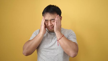 Téléchargez les photos : Jeune homme chinois souffrant de maux de tête sur fond jaune isolé - en image libre de droit