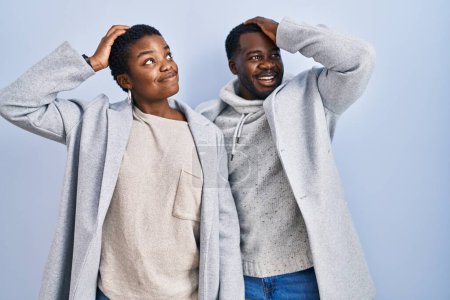 Téléchargez les photos : Jeune couple afro-américain debout sur fond bleu ensemble souriant cheveux touchants confiants avec geste de la main vers le haut, posant attrayant et à la mode - en image libre de droit