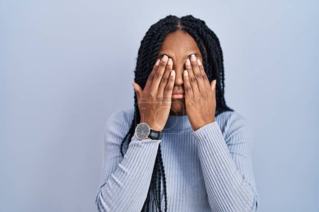 Foto de Mujer afroamericana de pie sobre fondo azul frotando los ojos para la fatiga y el dolor de cabeza, la expresión somnolienta y cansada. problema de visión - Imagen libre de derechos