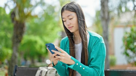 Foto de Joven mujer china usando teléfono inteligente con expresión seria en el parque - Imagen libre de derechos