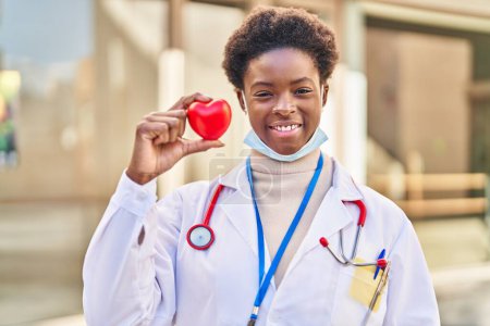 Foto de Mujer afroamericana vistiendo uniforme médico sosteniendo el corazón con aspecto positivo y feliz de pie y sonriendo con una sonrisa confiada mostrando los dientes - Imagen libre de derechos