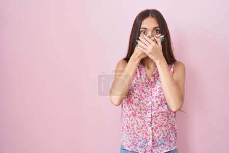 Photo for Young hispanic woman with long hair standing over pink background shocked covering mouth with hands for mistake. secret concept. - Royalty Free Image