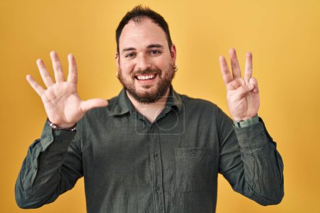 Photo for Plus size hispanic man with beard standing over yellow background showing and pointing up with fingers number eight while smiling confident and happy. - Royalty Free Image