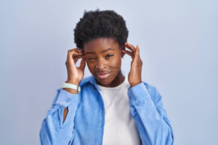 Photo for African american woman standing over blue background covering ears with fingers with annoyed expression for the noise of loud music. deaf concept. - Royalty Free Image