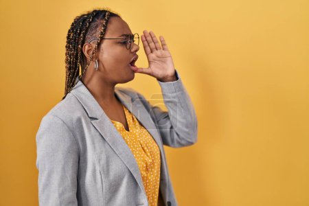 Téléchargez les photos : Femme afro-américaine avec des tresses debout sur fond jaune criant et criant fort à côté avec la main sur la bouche. concept de communication. - en image libre de droit