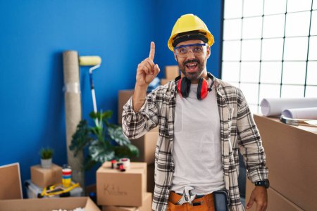 Foto de Joven hombre hispano con barba trabajando en la renovación del hogar apuntando con el dedo hacia arriba con una idea exitosa. exitado y feliz. número uno. - Imagen libre de derechos