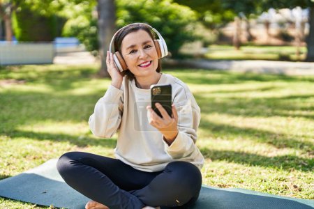 Téléchargez les photos : Femme d'âge moyen écoutant de la musique assise sur une herbe au parc - en image libre de droit