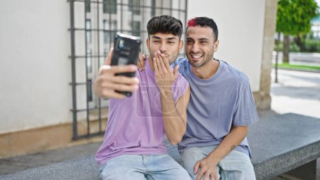 Téléchargez les photos : Deux hommes couple souriant confiant ayant appel vidéo à la rue - en image libre de droit