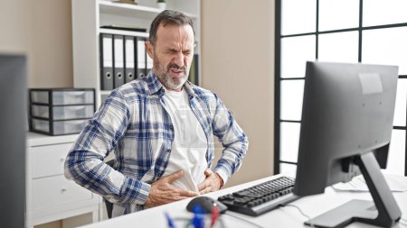 Foto de Hombre de mediana edad trabajador de negocios que sufre de dolor de estómago que trabaja en la oficina - Imagen libre de derechos