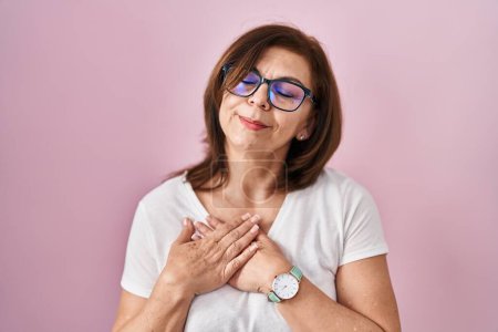 Photo for Middle age hispanic woman standing over pink background smiling with hands on chest with closed eyes and grateful gesture on face. health concept. - Royalty Free Image