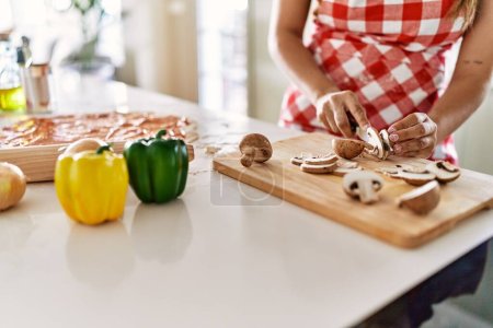 Photo for Young beautiful hispanic woman cutting mushroom at the kitchen - Royalty Free Image