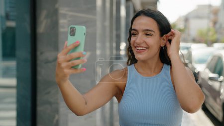 Foto de Joven hermosa mujer hispana sonriendo confiada haciendo selfie por el teléfono inteligente en la calle - Imagen libre de derechos
