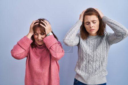 Téléchargez les photos : Mère et fille debout sur fond bleu souffrant de maux de tête désespérés et stressés parce que la douleur et la migraine. mains sur la tête. - en image libre de droit