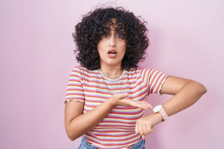 Téléchargez les photos : Jeune femme du Moyen-Orient debout sur fond rose pressé pointant pour regarder le temps, l'impatience, bouleversé et en colère pour retard de délai - en image libre de droit