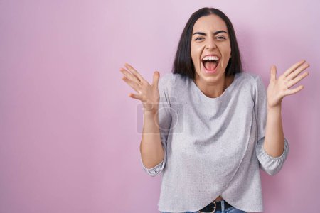 Téléchargez les photos : Young brunette woman standing over pink background celebrating crazy and amazed for success with arms raised and open eyes screaming excited. winner concept - en image libre de droit