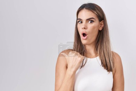 Photo for Hispanic young woman standing over white background surprised pointing with hand finger to the side, open mouth amazed expression. - Royalty Free Image