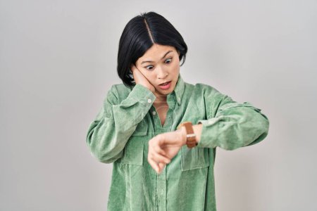 Téléchargez les photos : Jeune femme asiatique debout sur fond blanc regardant le temps de la montre inquiet, peur d'arriver en retard - en image libre de droit