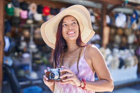 Téléchargez les photos : Jeune belle hispanique femme touriste en utilisant une caméra vintage au marché de la rue - en image libre de droit