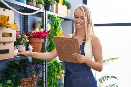 Photo for Young blonde woman florist smiling confident organize shelving at florist store - Royalty Free Image