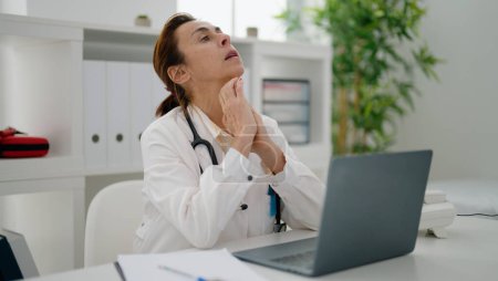 Foto de Mujer hispana de mediana edad vistiendo uniforme médico estresado trabajando en clínica - Imagen libre de derechos