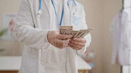 Foto de Joven médico hispano contando dólares en la clínica - Imagen libre de derechos