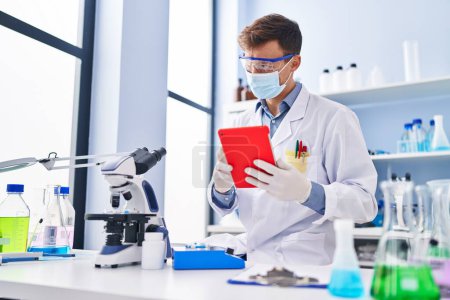 Photo for Young man scientist wearing medical mask using touchpad at laboratory - Royalty Free Image