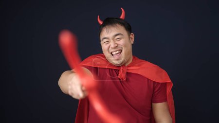 Téléchargez les photos : Jeune homme chinois portant costume diable tenant trident sur fond noir isolé - en image libre de droit