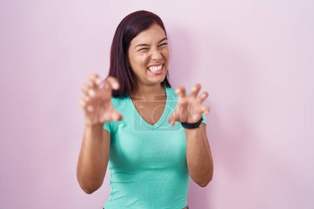 Téléchargez les photos : Jeune femme hispanique debout sur fond rose souriant drôle faisant griffe geste comme chat, expression agressive et sexy - en image libre de droit