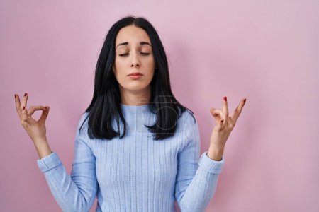 Téléchargez les photos : Femme hispanique debout sur fond rose détendue et souriante avec les yeux fermés faisant geste de méditation avec les doigts. concept de yoga. - en image libre de droit