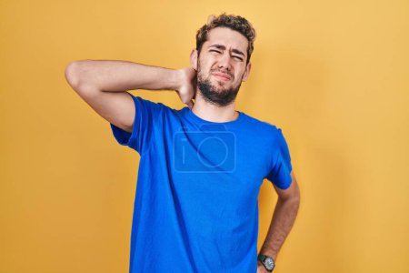 Photo for Hispanic man with beard standing over yellow background suffering of neck ache injury, touching neck with hand, muscular pain - Royalty Free Image