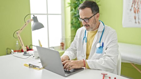 Photo for Middle age man doctor using laptop working at clinic - Royalty Free Image