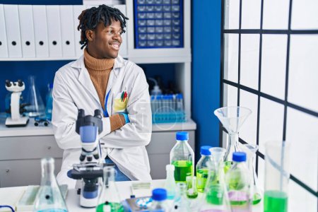 Téléchargez les photos : Homme scientifique afro-américain assis avec les bras croisés geste au laboratoire - en image libre de droit