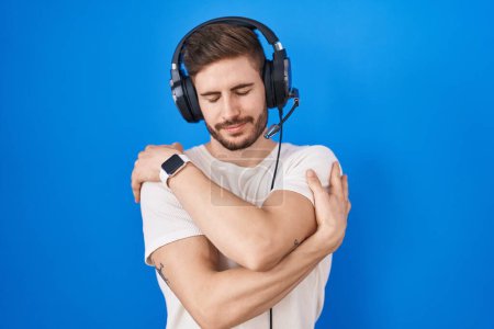 Photo for Hispanic man with beard listening to music wearing headphones hugging oneself happy and positive, smiling confident. self love and self care - Royalty Free Image