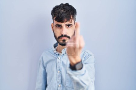 Photo for Young hispanic man with beard standing over blue background showing middle finger, impolite and rude fuck off expression - Royalty Free Image
