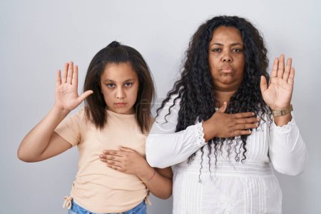 Photo for Mother and young daughter standing over white background swearing with hand on chest and open palm, making a loyalty promise oath - Royalty Free Image
