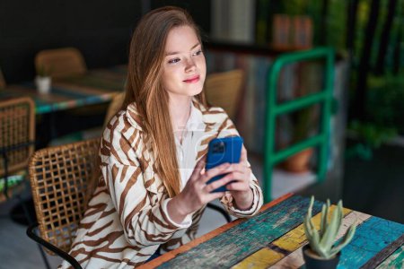 Téléchargez les photos : Jeune femme caucasienne utilisant smartphone assis sur la table au restaurant - en image libre de droit