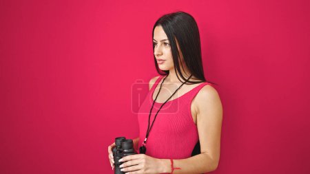 Téléchargez les photos : Jeune belle femme hispanique sauveteur tenant des jumelles avec expression détendue sur fond rouge isolé - en image libre de droit