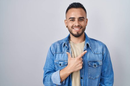 Téléchargez les photos : Jeune homme hispanique debout sur fond isolé gai avec un sourire sur le visage pointant avec la main et le doigt vers le côté avec une expression heureuse et naturelle - en image libre de droit
