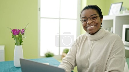 Photo for African american woman using laptop sitting on table at dinning room - Royalty Free Image