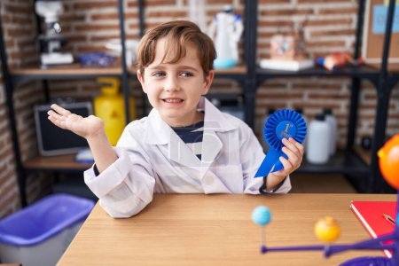 Téléchargez les photos : Petit garçon caucasien au laboratoire scientifique de l'école gagnant le premier prix célébrant la réalisation avec sourire heureux et expression gagnante avec la main levée - en image libre de droit