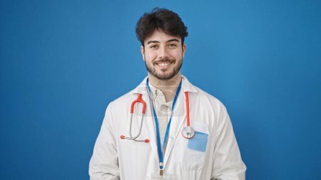 Photo for Young hispanic man doctor smiling confident standing over isolated blue background - Royalty Free Image