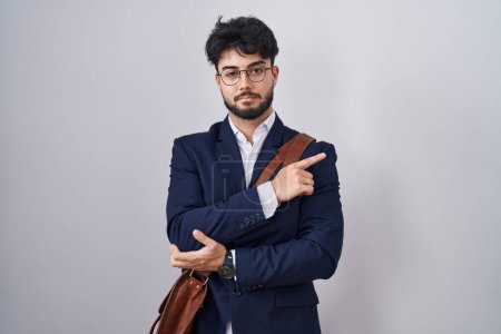 Foto de Hombre hispano con barba llevando ropa de negocios apuntando con el dedo de la mano hacia un lado mostrando publicidad, cara seria y tranquila - Imagen libre de derechos