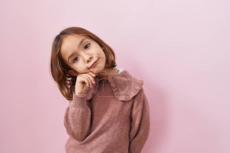 Photo for Little hispanic girl standing over pink background serious face thinking about question with hand on chin, thoughtful about confusing idea - Royalty Free Image
