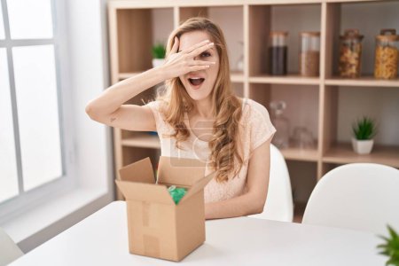Photo for Beautiful blonde woman with cardboard box peeking in shock covering face and eyes with hand, looking through fingers afraid - Royalty Free Image