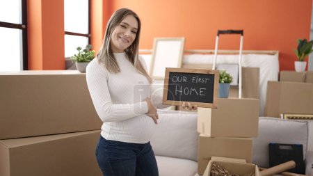 Photo for Young pregnant woman touching belly holding blackboard at new home - Royalty Free Image